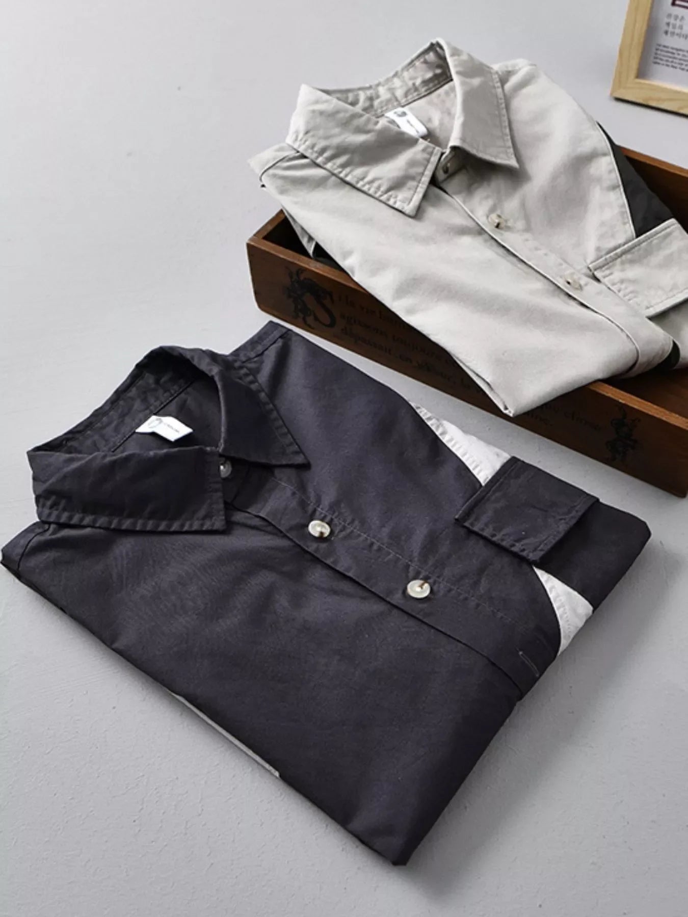 Two folded men's streetwear shirts, one black with white accents, one beige, on light background