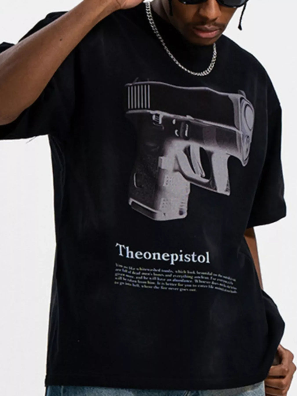 Man wearing a black oversized streetwear t-shirt with large graphic pistol print and silver chain