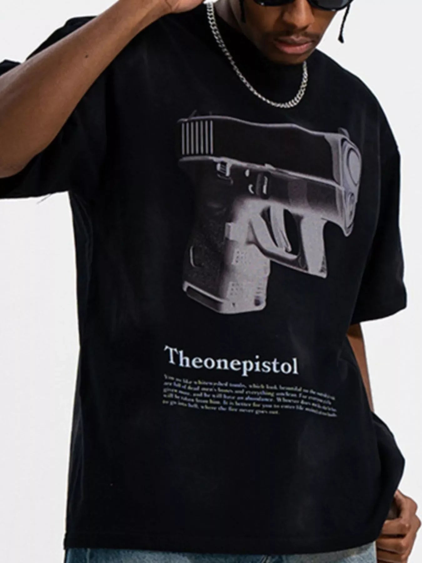 Man wearing a black oversized streetwear t-shirt with large graphic pistol print and silver chain