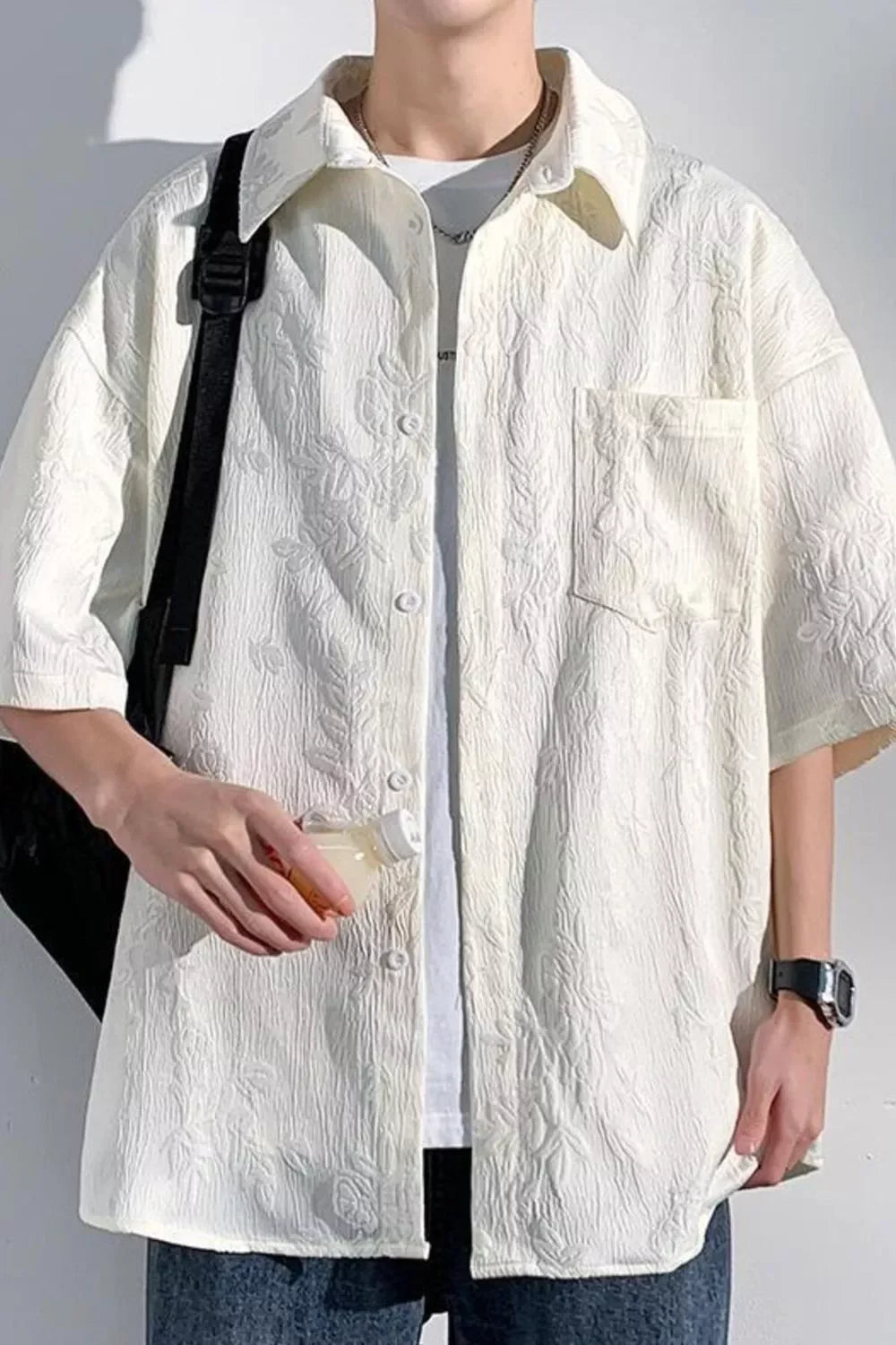 Man in oversized textured white short-sleeve shirt, streetwear style, holding drink