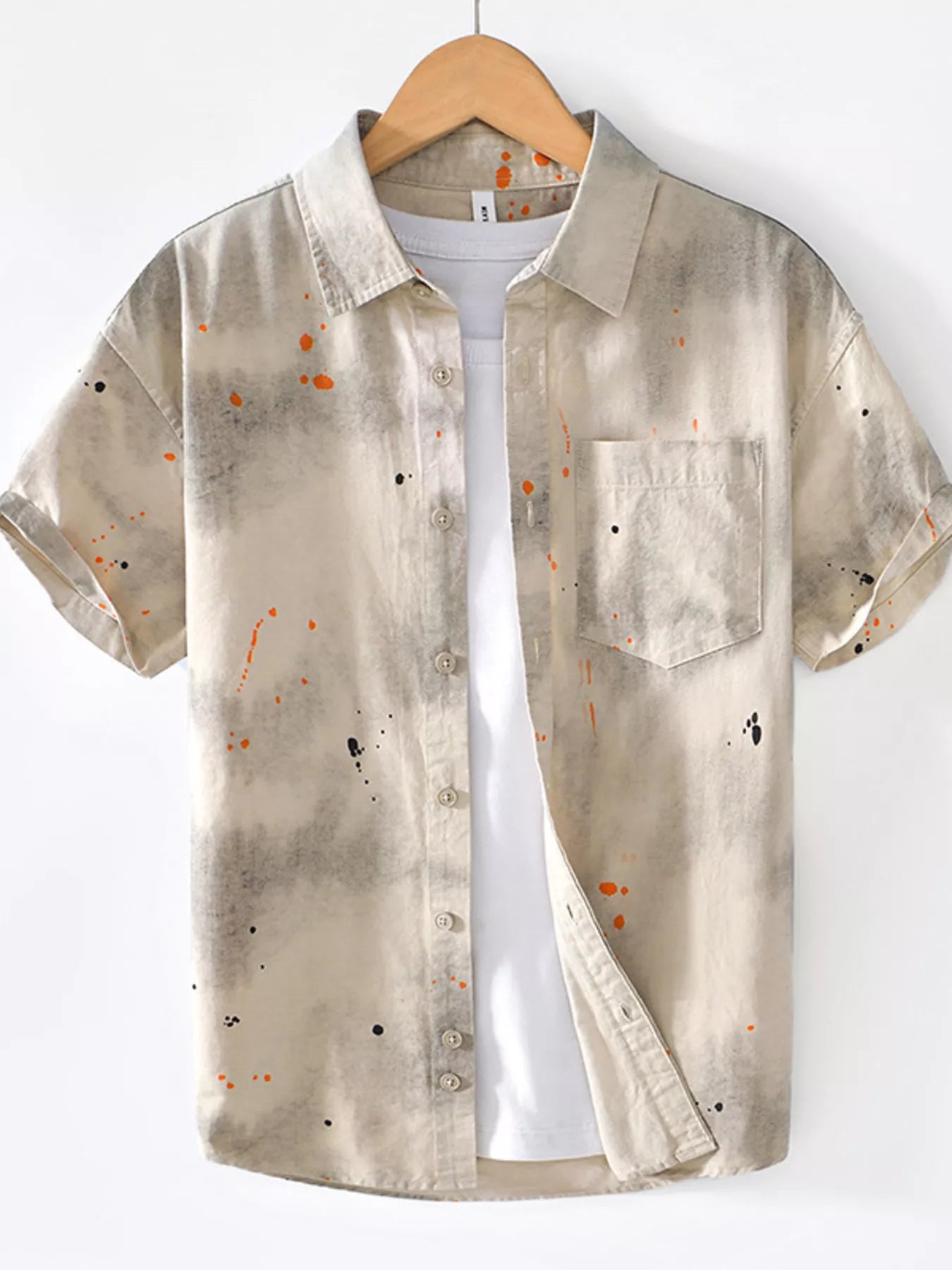 Beige short-sleeve streetwear shirt with paint splatter, front pocket, and urban casual style.