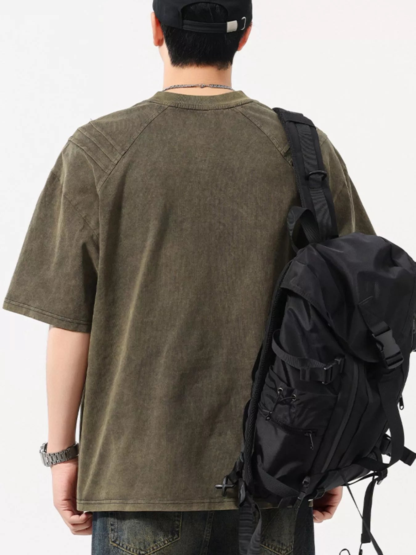 Man wearing an oversized khaki streetwear t-shirt, black cap and backpack, back view