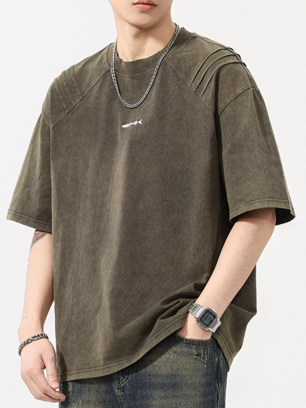 Man wearing oversized khaki streetwear t-shirt with small graphic, casual jeans, and silver accessories
