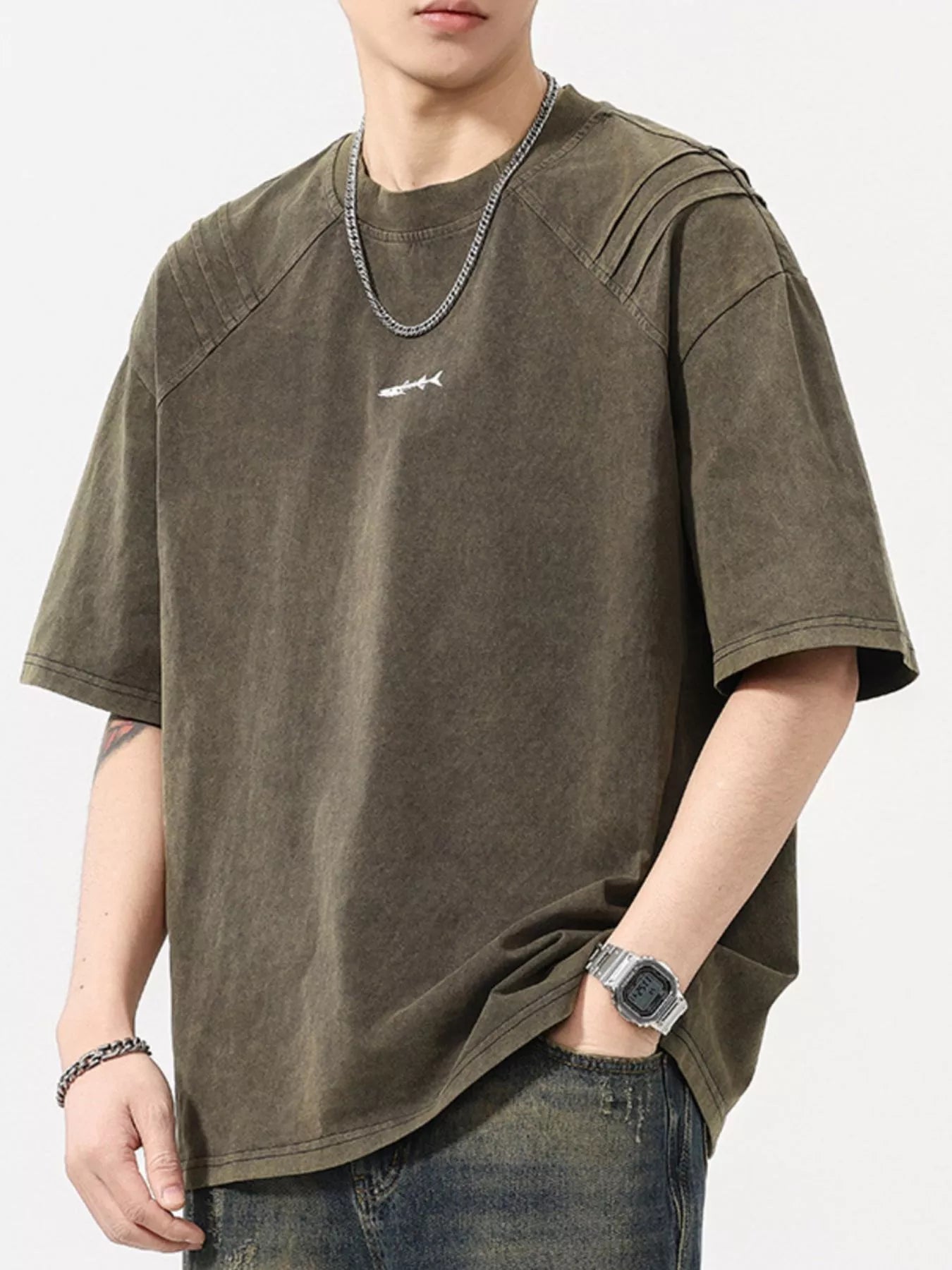 Man wearing oversized khaki streetwear t-shirt with small graphic, casual jeans, and silver accessories
